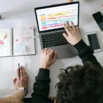Deux personnes collaborant sur un ordinateur portable et un agenda à un bureau moderne et dynamique.
