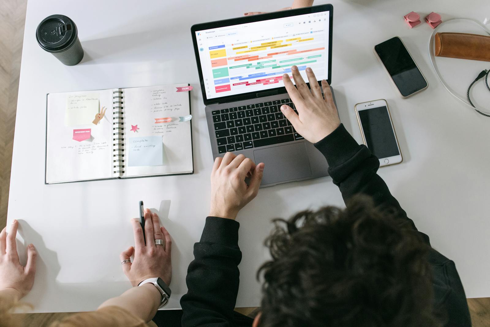 Deux personnes collaborant sur un ordinateur portable et un agenda à un bureau moderne et dynamique.